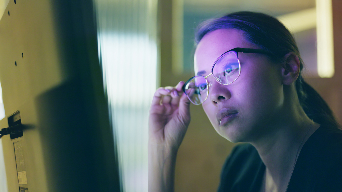 Close-up image of an Asian woman studying information on a computer screen.
She’s in a small office with the screen lighting up her face.